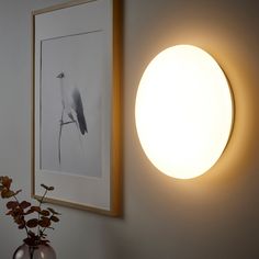 a light that is on the wall next to a vase with some flowers in it