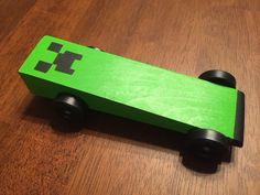 a green toy car sitting on top of a wooden floor next to a black object