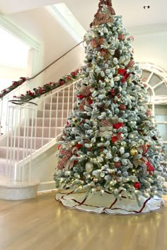 a decorated christmas tree sitting in the middle of a living room next to a stair case