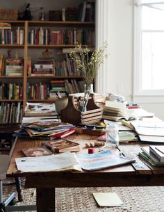 a wooden table topped with lots of books next to a tall book shelf filled with books