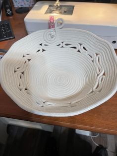 a white bowl sitting on top of a wooden table next to a sewing machine and needle