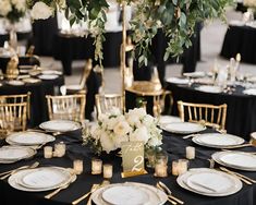 the table is set with black linens, gold chargers and white flowers