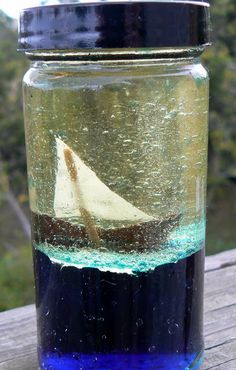 a glass jar filled with blue liquid and a white sailboat