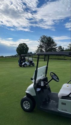 two golf carts parked in the grass on a sunny day with blue skies and white clouds