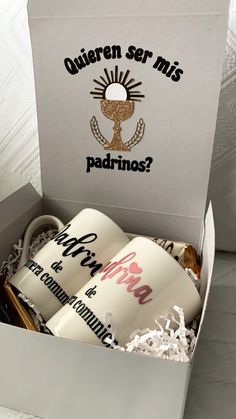 two coffee mugs in a box with the words quieren ser miss padrinos