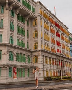 a woman is standing in front of a building with many windows and colorful shutters