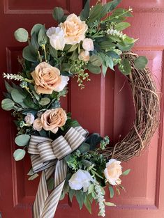 a wreath with flowers and greenery hanging on a red front door by a striped ribbon