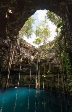 the inside of a cave with blue water and trees on either side, as seen from below