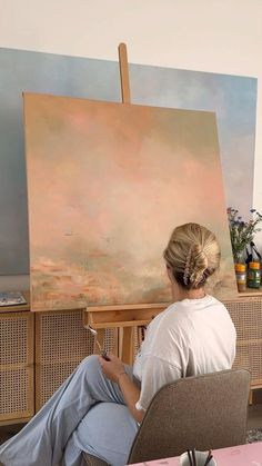 a woman sitting in front of an easel painting