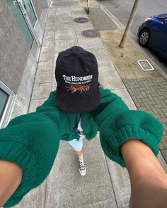 a person wearing a black hat and green pants is standing on the sidewalk in front of a building