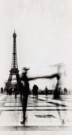 two people are dancing in front of the eiffel tower with their arms stretched out