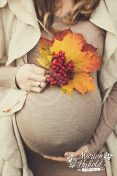 a pregnant woman wearing a sweater and holding a maple leaf with berries on it's belly