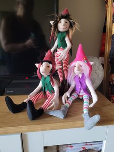 three dolls sitting on top of a wooden table in front of a flat screen tv