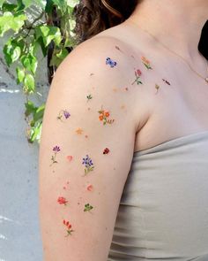 a woman with flowers painted on her arm and shoulder, standing next to a plant