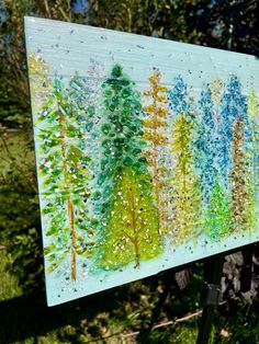 a painting on a easel in the grass with trees painted on it and sprinkles all over