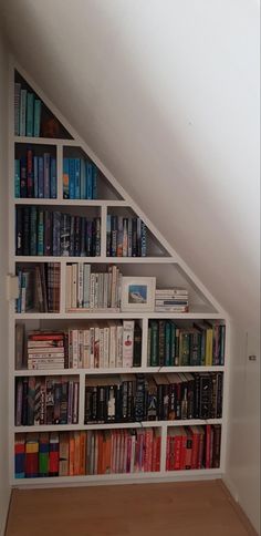 a book shelf filled with lots of books on top of a wooden floor next to a white wall