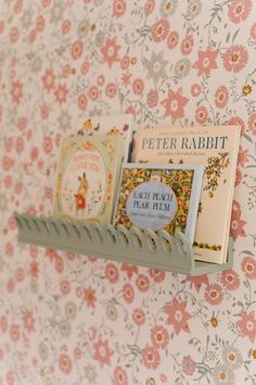 there is a book rack on the wall with some books in front of it and a flowered wall paper behind it