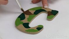 someone is painting the letter c with green and brown camouflage print on it's surface