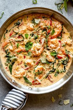 a pan filled with shrimp and spinach on top of a gray table next to a striped napkin