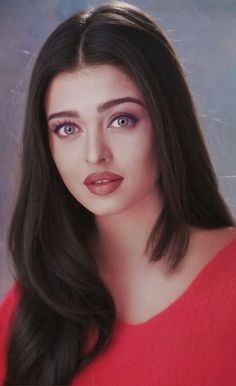 a woman with long dark hair wearing a red shirt and posing for a photo in front of a blue background