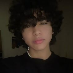 a woman with curly hair wearing a black shirt and pearl necklace looking at the camera