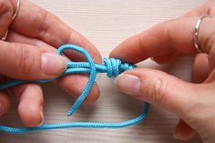 two hands are tying a blue string together