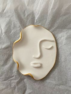 a white and gold plate with a face painted on the side, sitting on a piece of paper