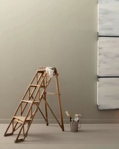 a ladder leaning up against a wall next to a bucket and paint roller on the floor