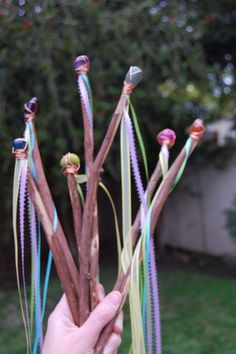 a hand is holding up several branches with ribbons attached to them in front of some bushes