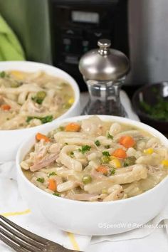 two bowls of chicken noodle soup on a table with a crock pot in the background