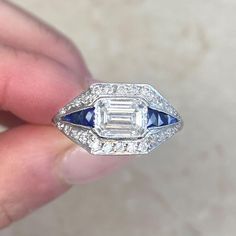 a woman's hand holding an antique diamond and sapphire engagement ring with blue accents