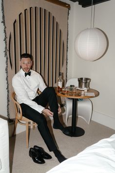 a man in a tuxedo sitting on a chair next to a small table