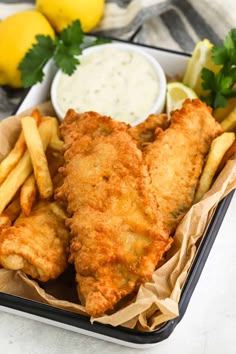 fried fish and fries in a tray with lemon wedges