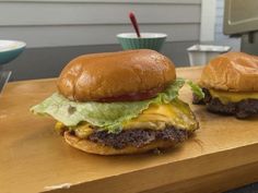 two hamburgers sitting on top of a wooden cutting board