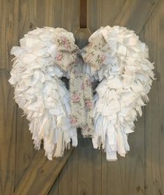 an angel wings hanging on the side of a wooden wall with flowers and leaves around it