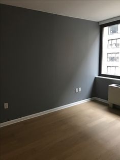 an empty room with hard wood flooring and gray painted walls in front of a window