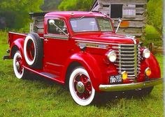 an old red truck is parked in the grass