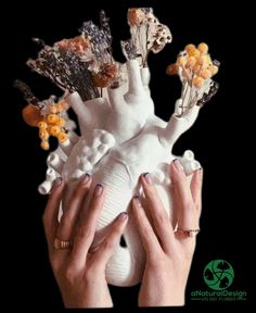 two hands holding up a white vase with flowers on it