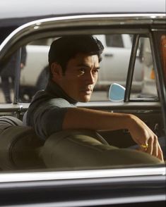 a man sitting in the passenger seat of a car with his hand on the steering wheel