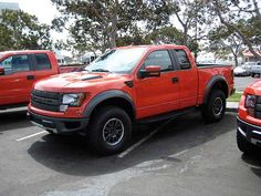 an orange pick up truck parked in a parking lot next to other red pickup trucks