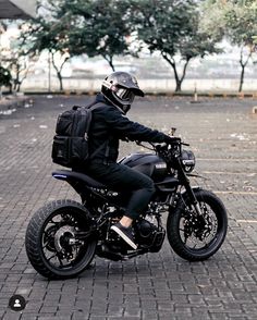 a person wearing a helmet and sitting on a black motorbike with trees in the background