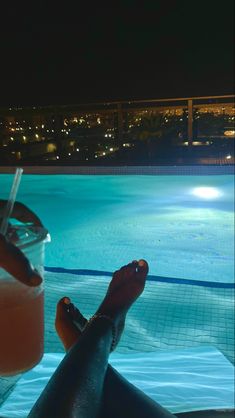 a person sitting in front of a pool at night with their feet on the edge