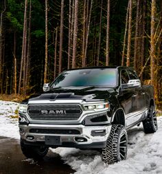 a black truck is driving through the snow in front of some trees and pine trees