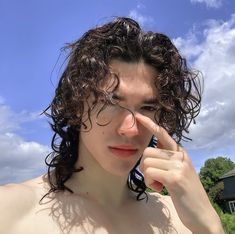 a man with curly hair and glasses holding a cell phone to his face while standing in front of a house