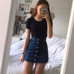 a young woman taking a selfie in her bedroom while wearing a black shirt and denim skirt