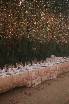 an outdoor dinner table set up with white linens and pink napkins, surrounded by string lights