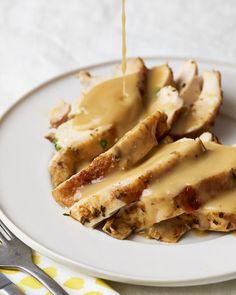 a white plate topped with sliced chicken covered in gravy and being drizzled