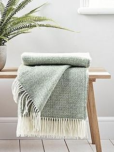 a green and white blanket sitting on top of a wooden bench next to a potted plant