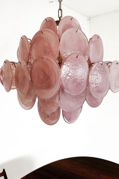 a pink chandelier hanging from a ceiling in a white room with a wooden table