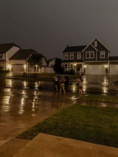 three children playing in the rain on a suburban street at night with their umbrellas open